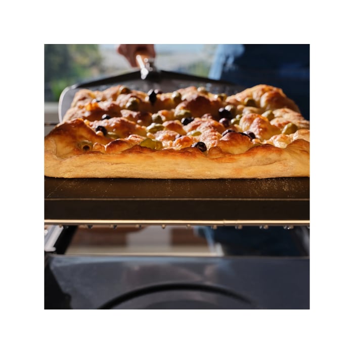 A focaccia baking inside the pizza expert oven with a pizza peel underneath 