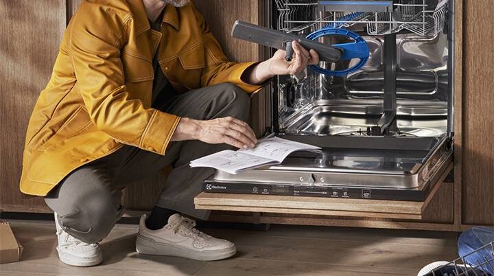 Person in front of open dishwasher with user manual
