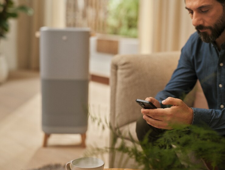 Mees hoiab telefoni ja istub õhupuhasti kõrval.