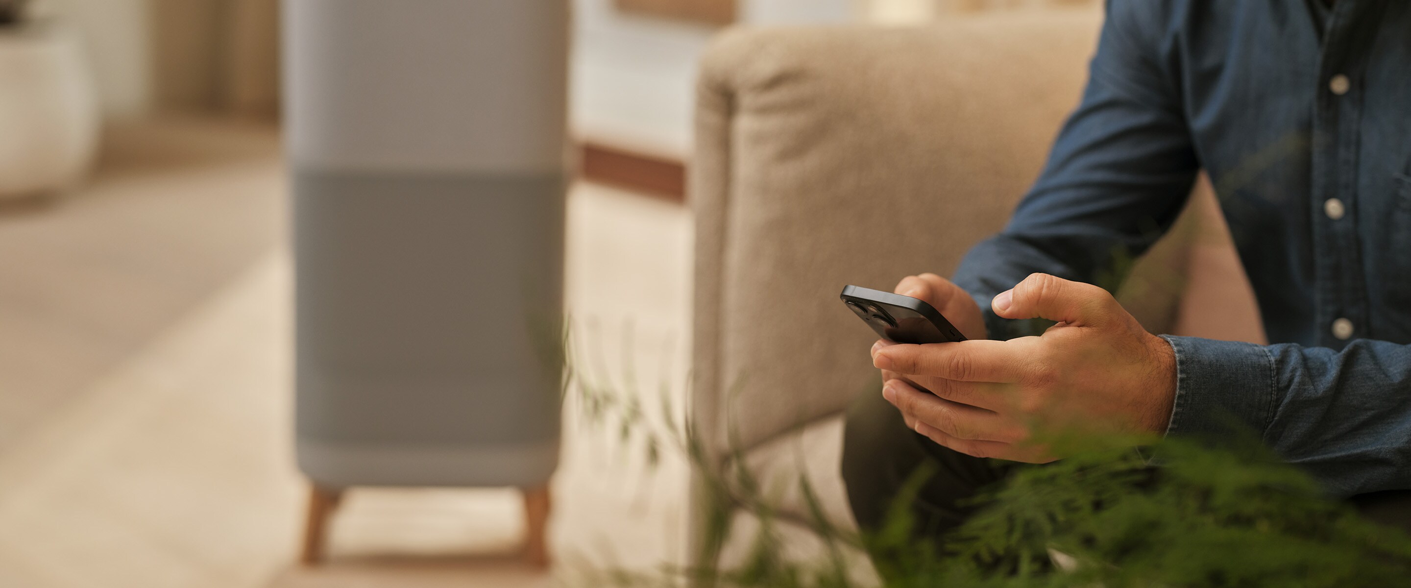 Mees istub ja hoiab telefoni käes. Taustal on õhupuhasti.